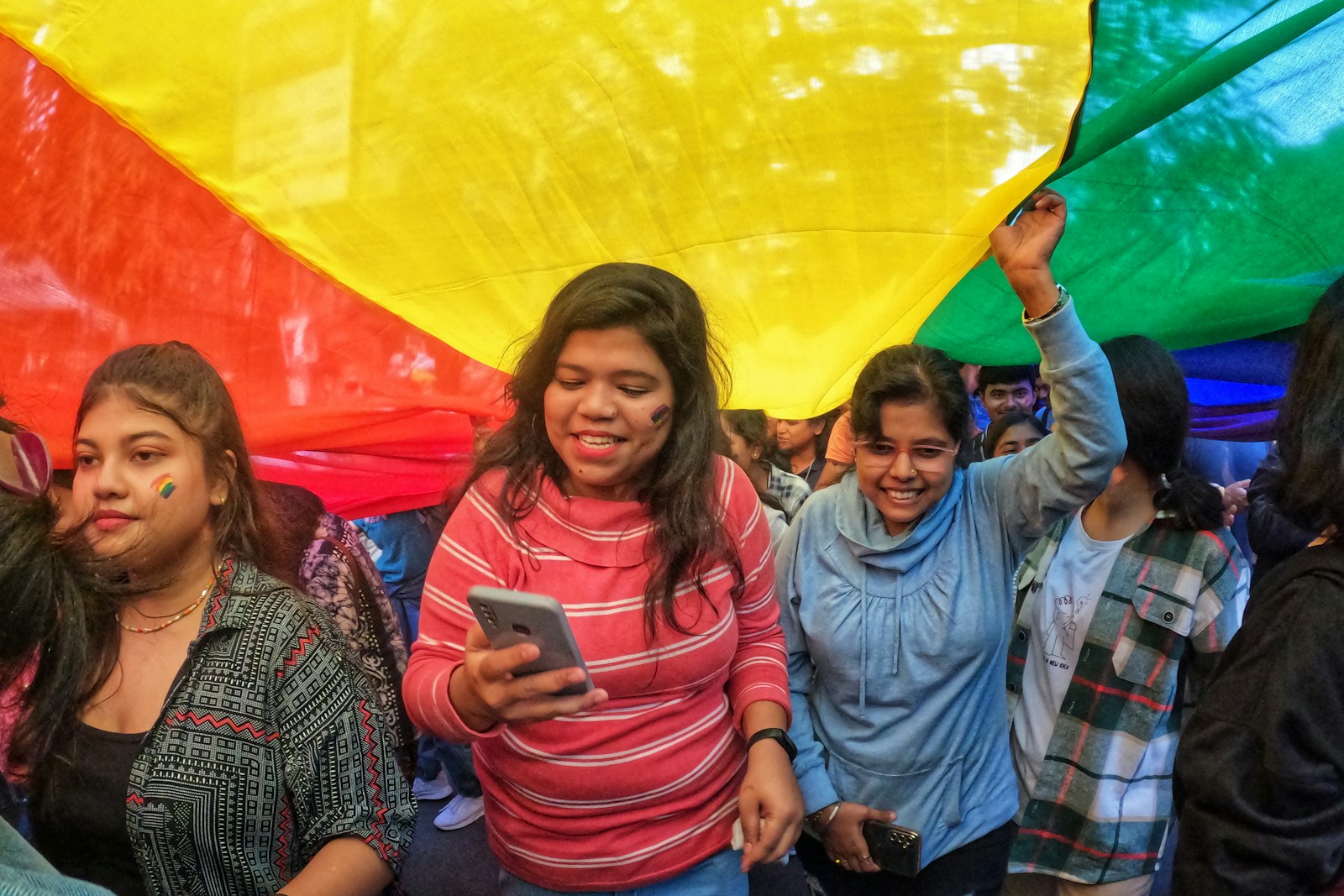 A group of people standing around a rainbow colored umbrella